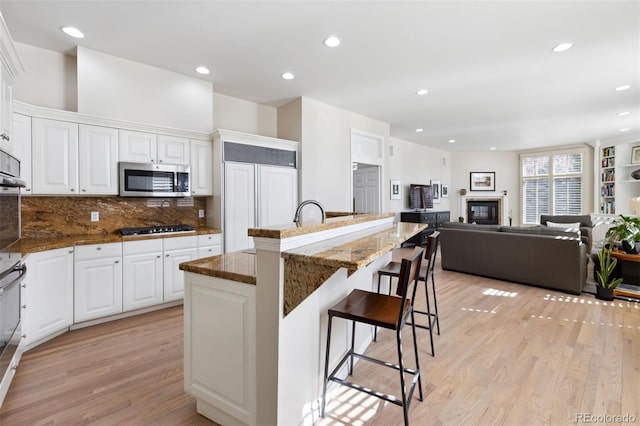 301 Garfield St Unit 1E, Denver, CO 80206 - kitchen with appliances with stainless steel finishes, light wood finished floors, a glass covered fireplace, a breakfast bar area, and dark stone countertops