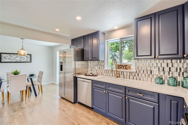 kitchen featuring decorative backsplash, stainless steel appliances, sink, light hardwood / wood-style floors, and hanging light fixtures