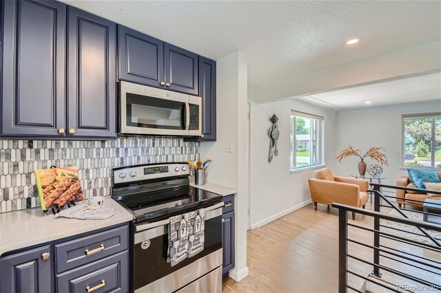 kitchen with blue cabinets, backsplash, a textured ceiling, appliances with stainless steel finishes, and light wood-type flooring