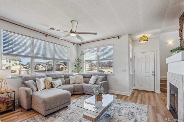 living area featuring a ceiling fan, baseboards, a fireplace, light wood-style floors, and a textured ceiling