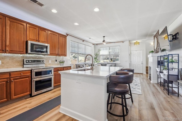 kitchen with visible vents, an island with sink, a sink, stainless steel appliances, and light countertops