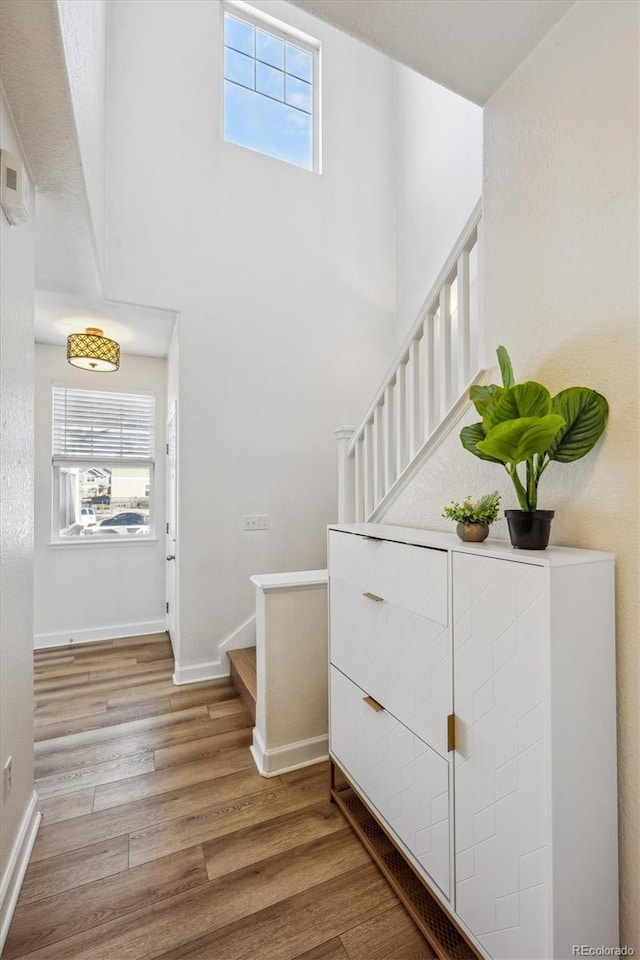 stairs with a wealth of natural light, a towering ceiling, baseboards, and wood finished floors