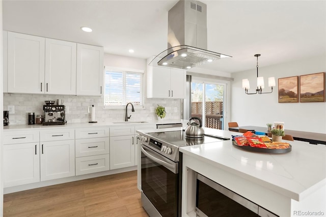 6163 W 76th Ave, Arvada, CO 80003 - kitchen with stainless steel range with electric cooktop, island range hood, light wood-style floors, white cabinetry, and backsplash