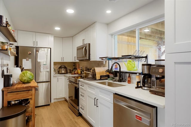 6163 W 76th Ave, Arvada, CO 80003 - kitchen featuring appliances with stainless steel finishes, white cabinetry, light wood finished floors, recessed lighting, and decorative backsplash