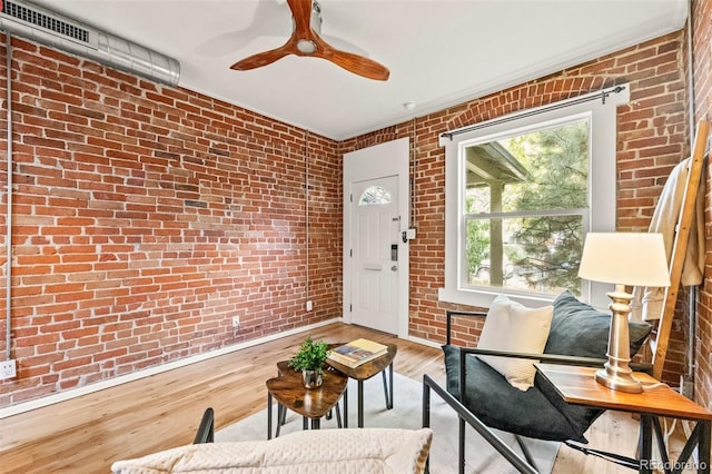 sitting room with brick wall, light hardwood / wood-style flooring, and ceiling fan