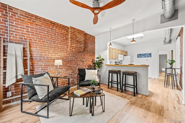 sitting room with ceiling fan, brick wall, and light hardwood / wood-style flooring