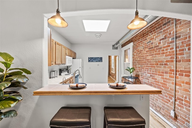 kitchen with hanging light fixtures, kitchen peninsula, brick wall, a breakfast bar, and a skylight