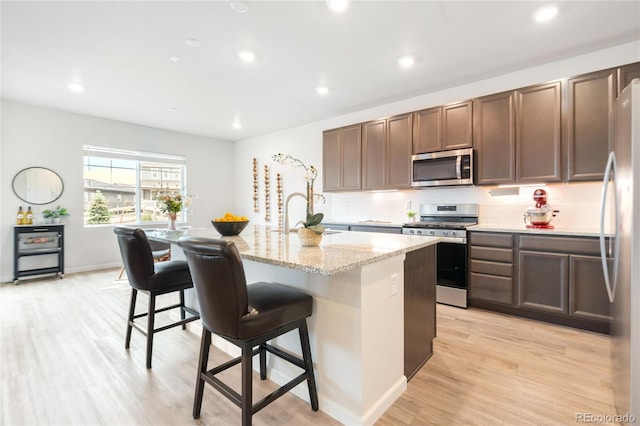 8582 Cheraw St, Littleton, CO 80125 - kitchen featuring stainless steel appliances, backsplash, light wood finished floors, a center island with sink, and recessed lighting