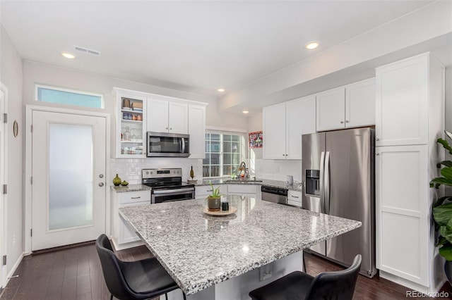 kitchen with stainless steel appliances, a kitchen island, a kitchen breakfast bar, decorative backsplash, and white cabinets