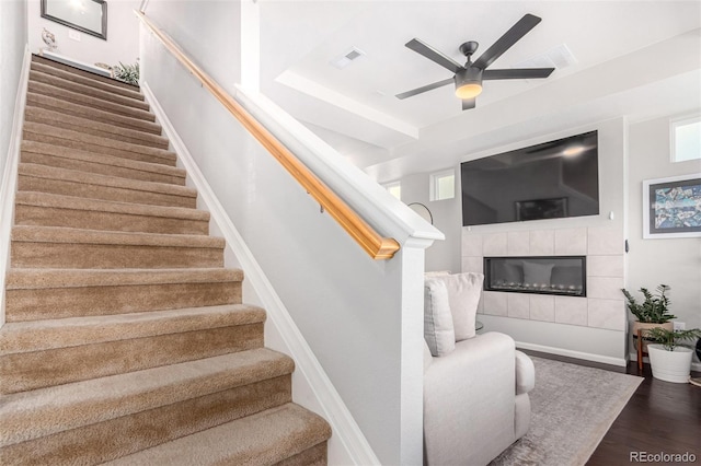 stairs with a tile fireplace, ceiling fan, plenty of natural light, and hardwood / wood-style flooring