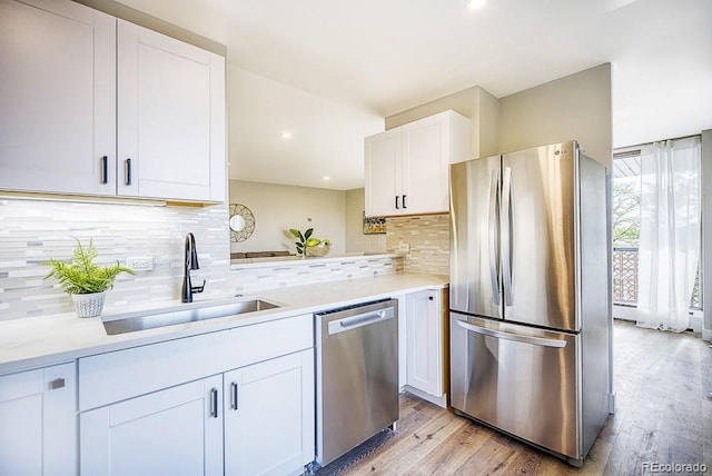 kitchen featuring sink, light hardwood / wood-style flooring, decorative backsplash, white cabinets, and appliances with stainless steel finishes