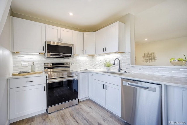 kitchen featuring white cabinetry, sink, backsplash, light hardwood / wood-style floors, and appliances with stainless steel finishes