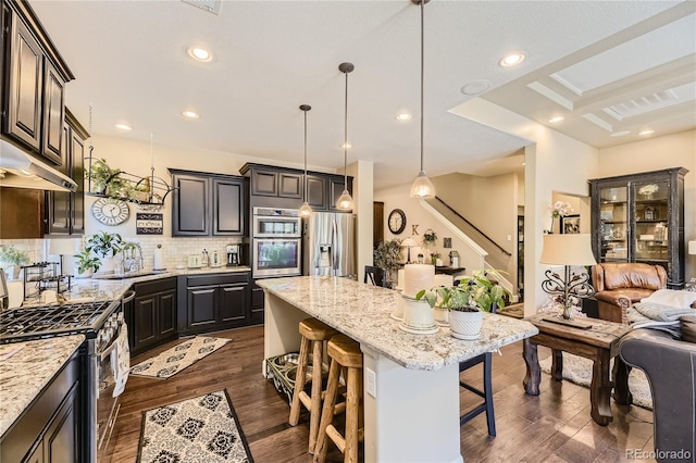 kitchen featuring light stone countertops, pendant lighting, appliances with stainless steel finishes, a kitchen island, and a breakfast bar