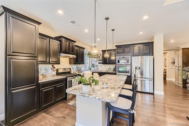 kitchen with decorative light fixtures, a kitchen island, appliances with stainless steel finishes, a breakfast bar area, and light stone counters