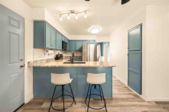 12234 W Saratoga Ave, Morrison, CO 80465 - kitchen with stainless steel appliances, blue cabinetry, a peninsula, light wood-type flooring, and a kitchen breakfast bar