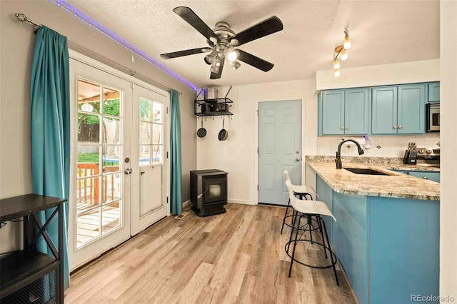 12234 W Saratoga Ave, Morrison, CO 80465 - kitchen with a breakfast bar area, a wood stove, blue cabinets, light wood-type flooring, and a textured ceiling