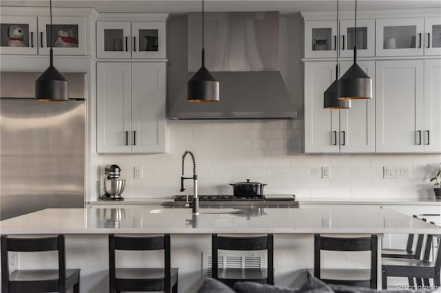 kitchen with white cabinetry, wall chimney exhaust hood, a kitchen bar, and hanging light fixtures