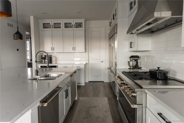 kitchen with pendant lighting, white cabinetry, sink, high end appliances, and wall chimney range hood