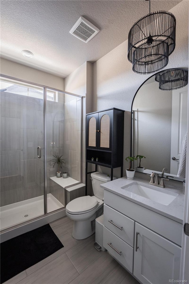 bathroom with vanity, toilet, a shower with shower door, and a textured ceiling