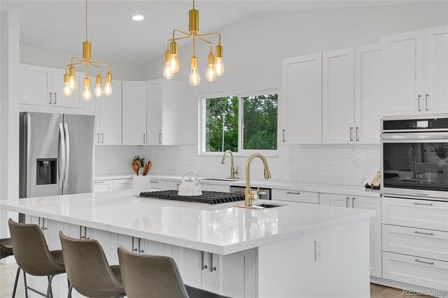 8357 Dudley Ct, Arvada, CO 80005 - kitchen with stainless steel appliances, a chandelier, an island with sink, backsplash, and vaulted ceiling
