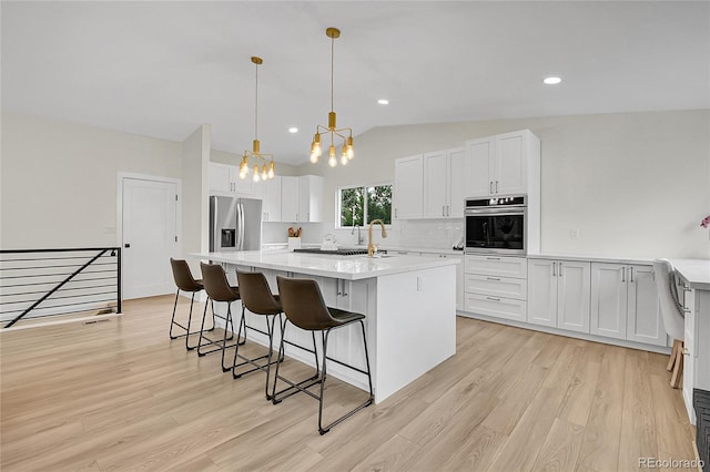 8357 Dudley Ct, Arvada, CO 80005 - kitchen featuring appliances with stainless steel finishes, lofted ceiling, light wood finished floors, light countertops, and a center island with sink