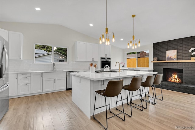 8357 Dudley Ct, Arvada, CO 80005 - kitchen with stainless steel appliances, lofted ceiling, light wood-style floors, white cabinetry, and light countertops