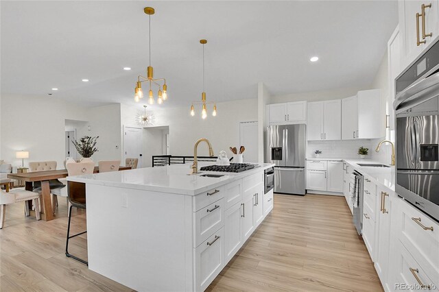 8357 Dudley Ct, Arvada, CO 80005 - kitchen with appliances with stainless steel finishes, light wood-type flooring, a center island with sink, a kitchen bar, and backsplash