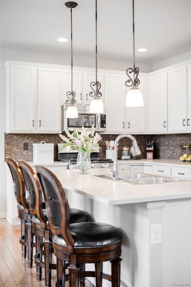 15205 W Baker Ave, Lakewood, CO 80228 - kitchen with stainless steel microwave, stove, white cabinets, hanging light fixtures, and a center island with sink