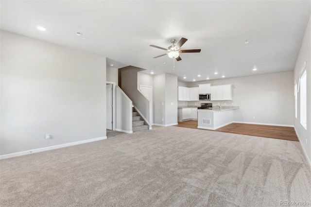 unfurnished living room featuring light colored carpet, ceiling fan, and sink