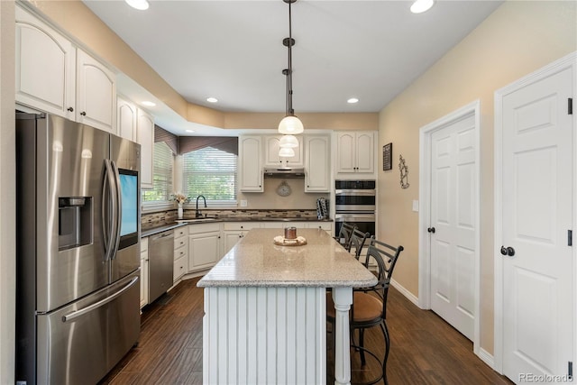 kitchen featuring a breakfast bar, a center island, appliances with stainless steel finishes, pendant lighting, and white cabinets