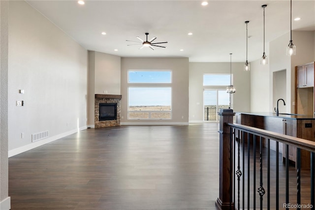 living room with sink, dark hardwood / wood-style flooring, a stone fireplace, and ceiling fan with notable chandelier