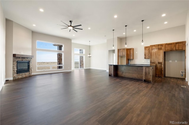 kitchen with a stone fireplace, a towering ceiling, ceiling fan, dark hardwood / wood-style floors, and decorative light fixtures