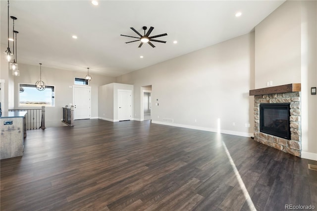 unfurnished living room featuring dark wood-type flooring, ceiling fan, and a stone fireplace