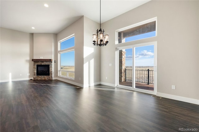 unfurnished living room with a notable chandelier, dark hardwood / wood-style flooring, and a stone fireplace