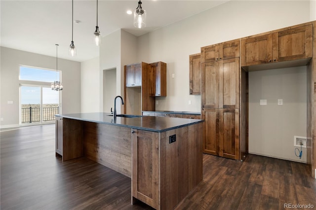 kitchen featuring dark wood-type flooring, hanging light fixtures, a center island with sink, a notable chandelier, and sink