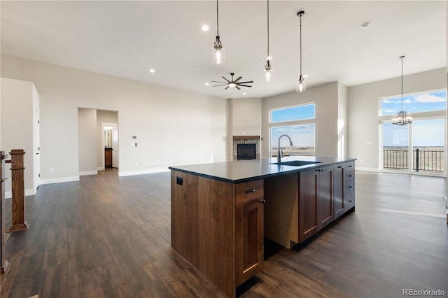 kitchen with pendant lighting, sink, a center island with sink, ceiling fan with notable chandelier, and a stone fireplace