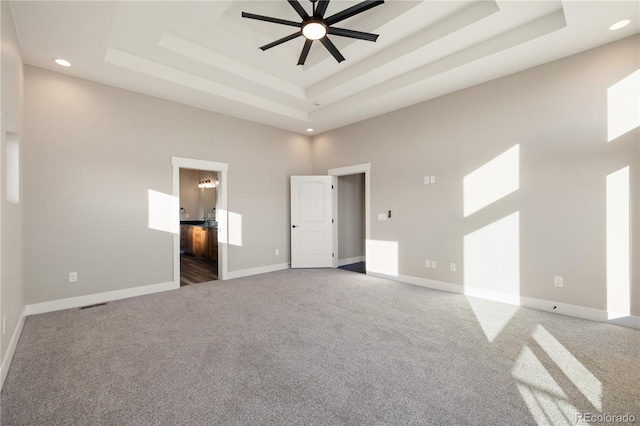 unfurnished bedroom with a high ceiling, ensuite bathroom, a tray ceiling, and carpet flooring