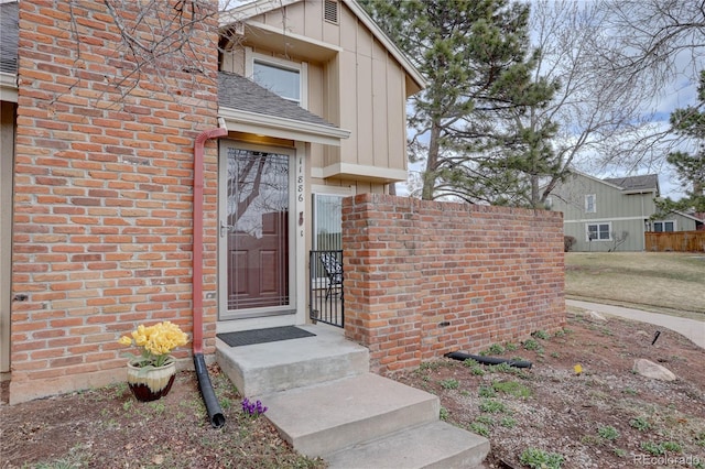 property entrance with roof with shingles, fence, board and batten siding, and brick siding