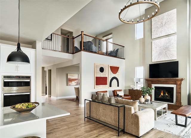 living room with a notable chandelier, a high ceiling, a glass covered fireplace, light wood-type flooring, and baseboards