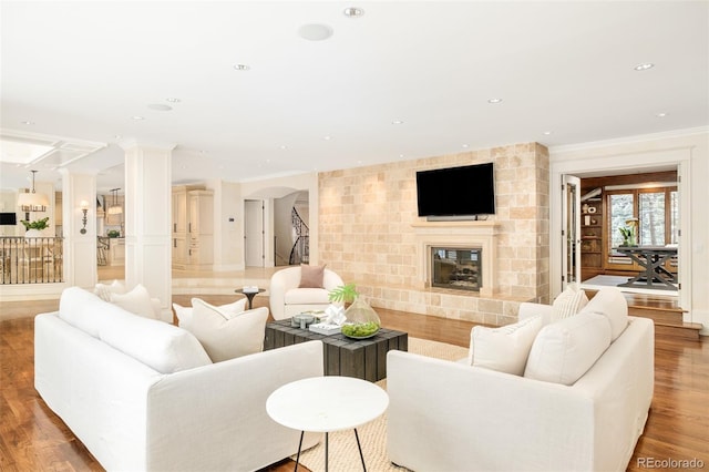 living room with hardwood / wood-style flooring, crown molding, a large fireplace, and ornate columns