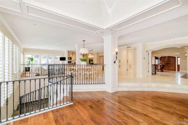 hall featuring a notable chandelier, ornamental molding, decorative columns, and light wood-type flooring