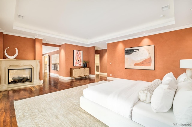 bedroom with a premium fireplace, wood-type flooring, and a tray ceiling