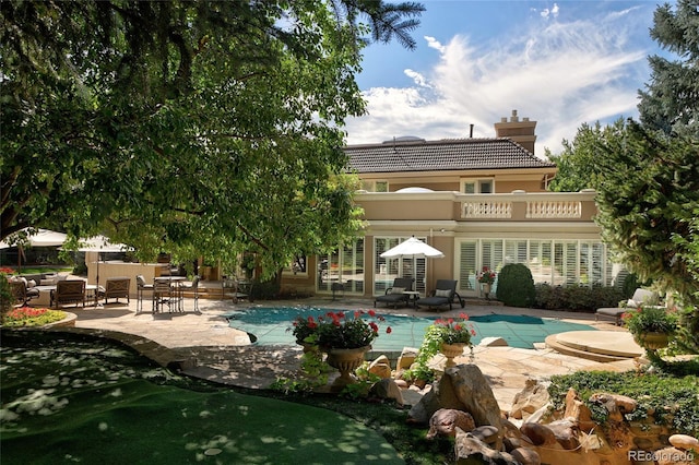 rear view of house featuring a balcony, a covered pool, and a patio area