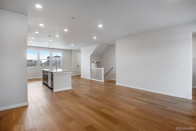 kitchen with an island with sink, sink, stainless steel dishwasher, and light hardwood / wood-style flooring