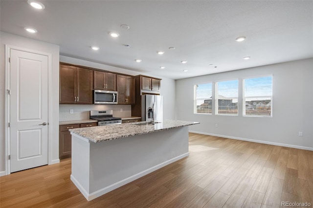 kitchen with a kitchen island with sink, light stone countertops, light hardwood / wood-style flooring, and stainless steel appliances