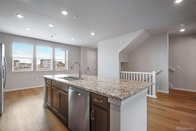 kitchen featuring an island with sink, sink, stainless steel appliances, dark brown cabinets, and light wood-type flooring