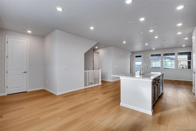 kitchen with a kitchen island with sink, sink, light stone counters, and light hardwood / wood-style floors