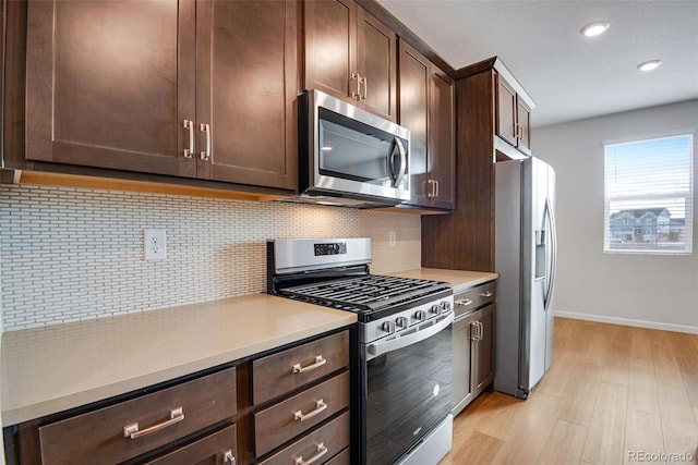 kitchen featuring dark brown cabinetry, backsplash, stainless steel appliances, and light wood-type flooring