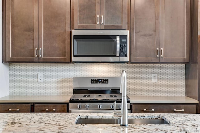 kitchen with tasteful backsplash, stainless steel appliances, sink, and light stone counters