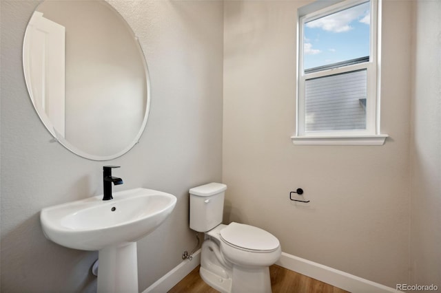 half bath featuring toilet, a sink, baseboards, and wood finished floors